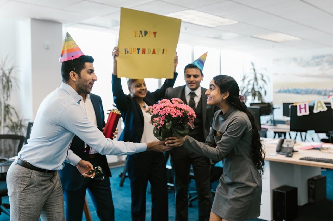 About Happy office birthday celebration with colleagues exchanging gifts and wearing party hats.